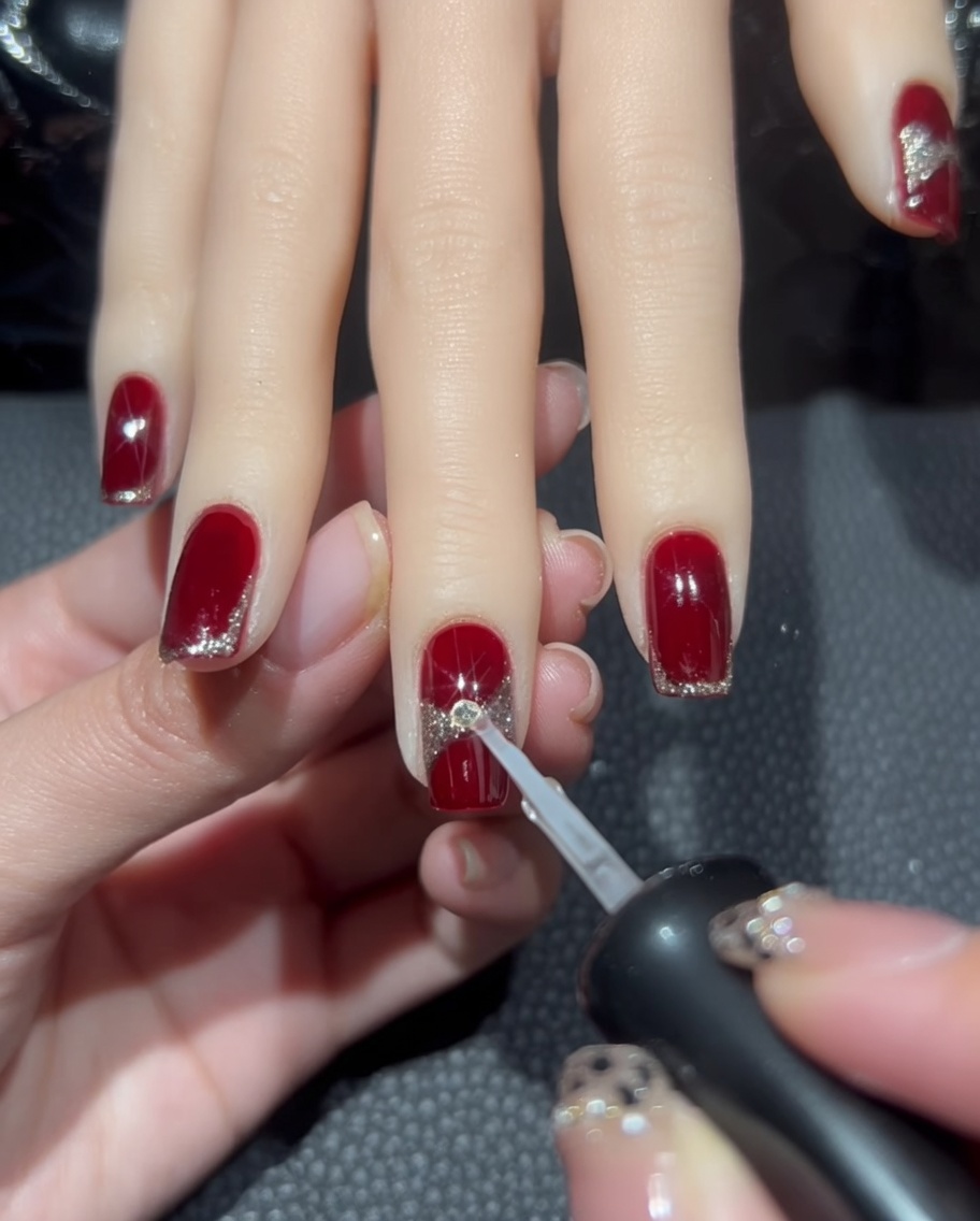 Ein kleiner Tropfen klarer Nagelkleber wird auf den Mittelpunkt des Glitter-Schleifendesigns gegeben.