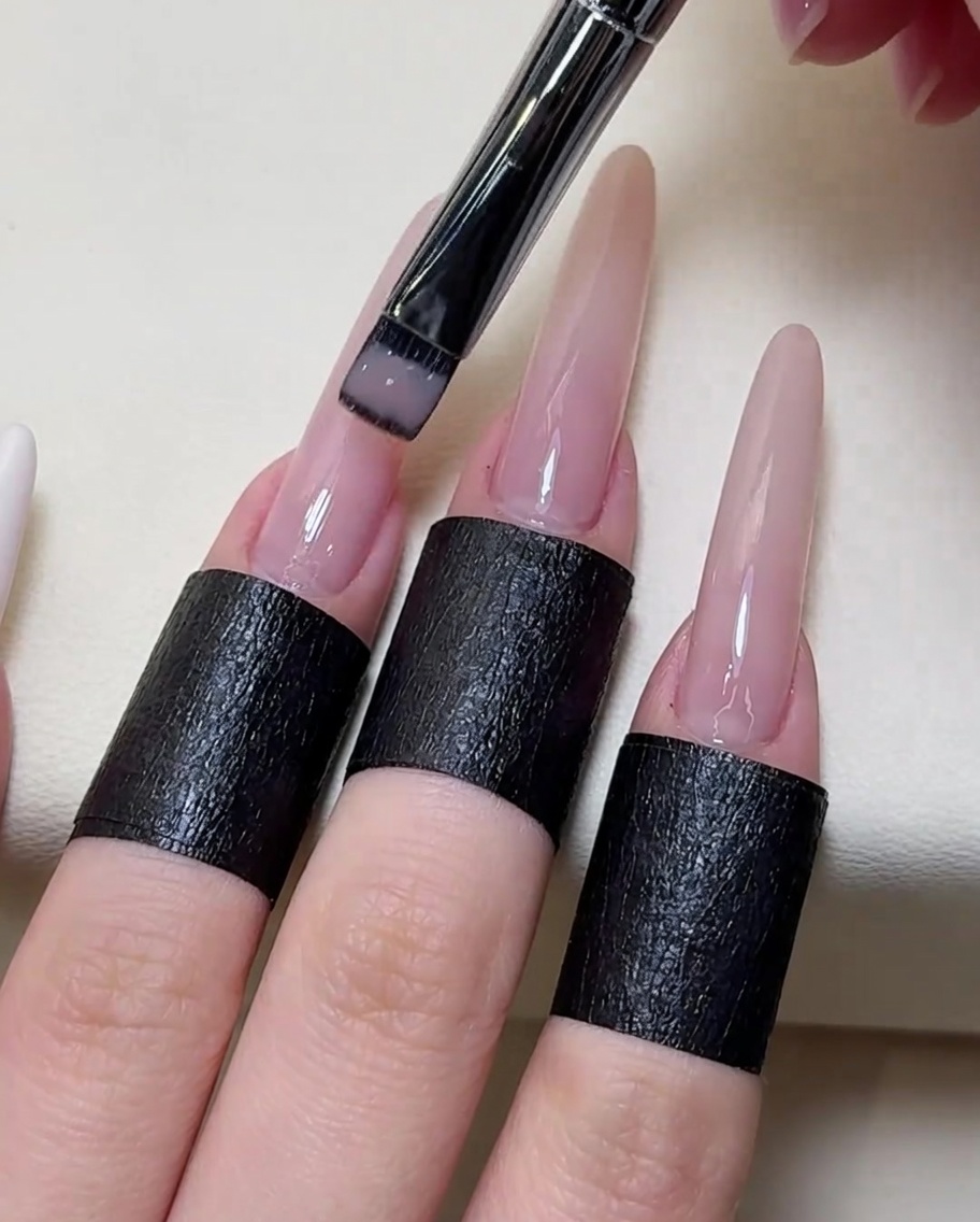 Nahaufnahme eines Pinsels, der transparentes Nude-Gel auf die Nagelplatte aufträgt.