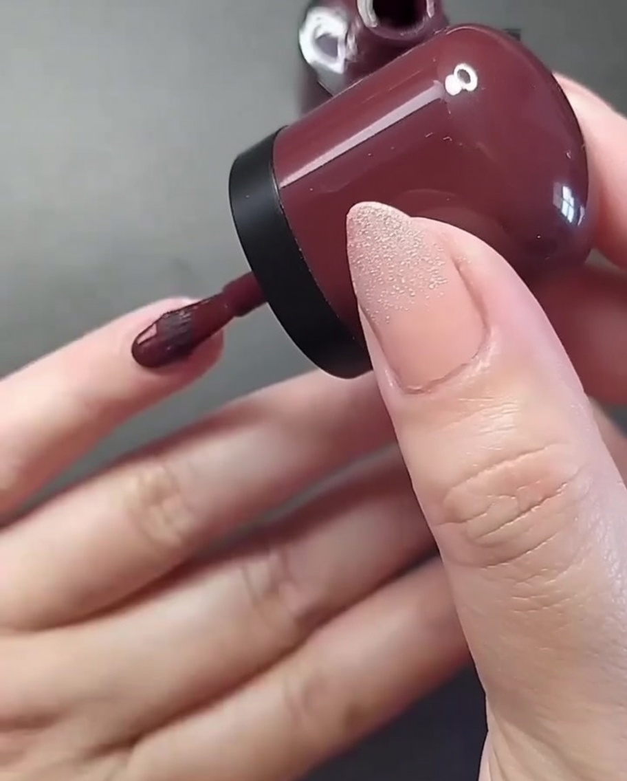 Nahaufnahme einer Hand, die tiefroten Nagellack auf den kleinen Fingernagel aufträgt.