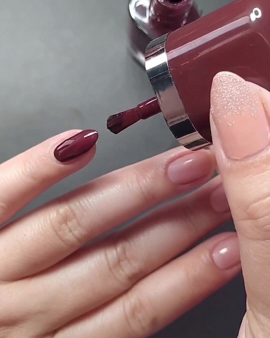 Nahaufnahme beim Auftragen von hellbeigem Nagellack auf den Ringfingernagel.