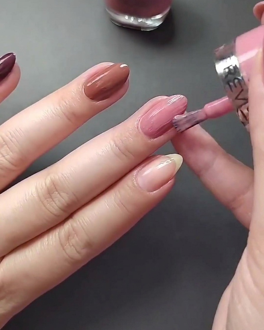 Nahaufnahme beim Auftragen von hellem Nude-Nagellack auf den Daumennagel.