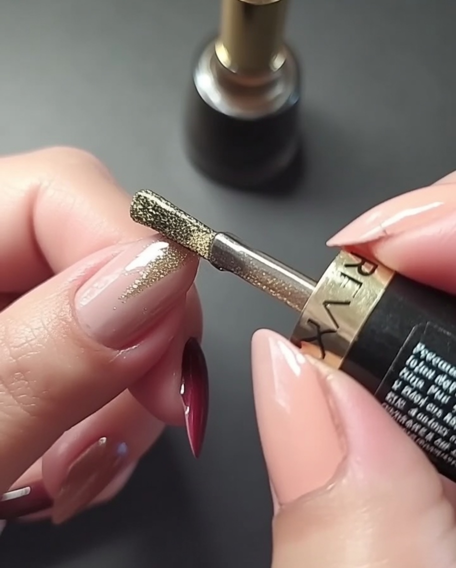 Nahaufnahme einer Hand, die eine präzise vertikale Goldlinie mittig auf einen rosenfarben manikürten Fingernagel malt.