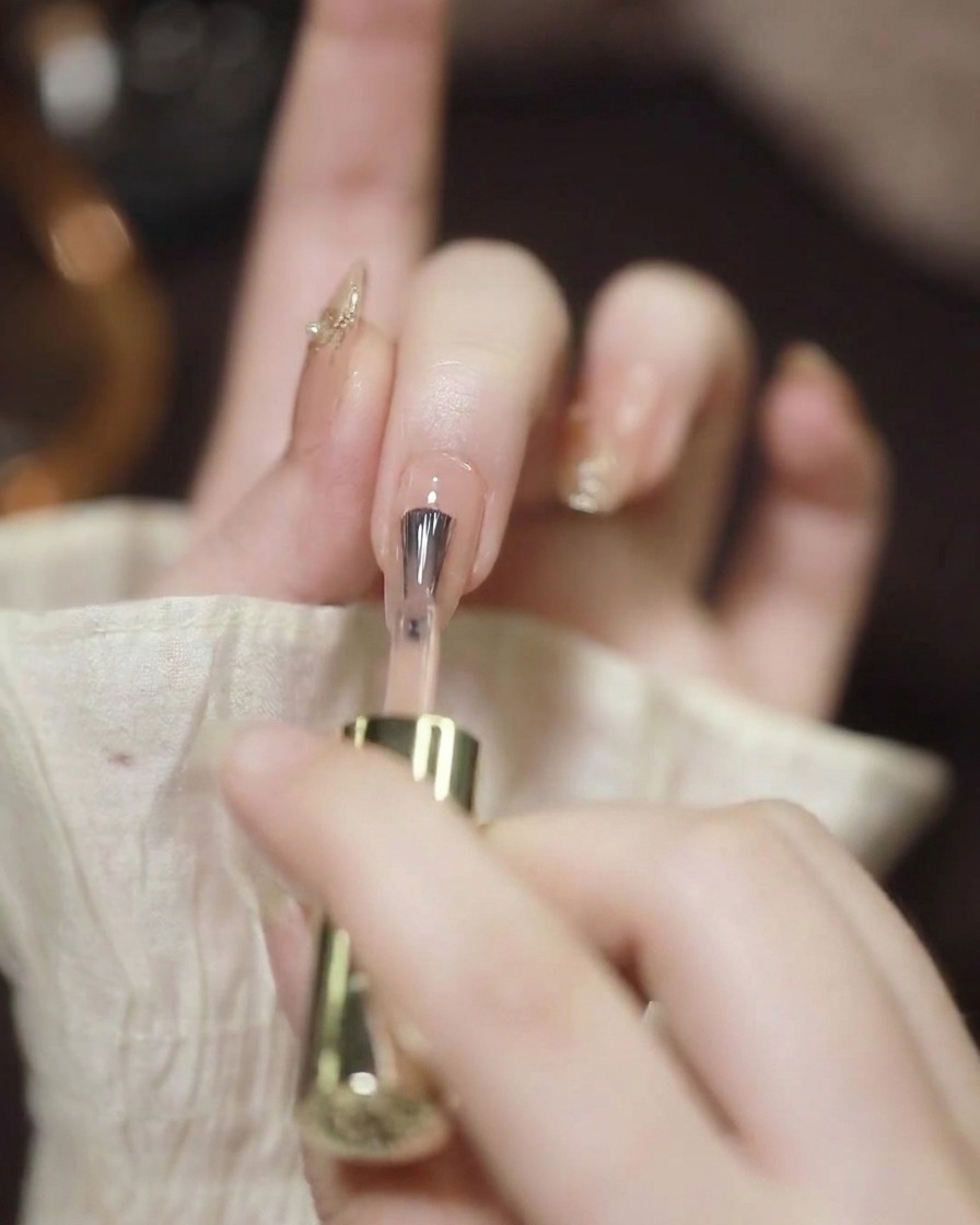 Nahaufnahme eines Nagelpinsels, der einen transparenten Nude-Gellack auf einen vorbereiteten Fingernagel aufträgt.