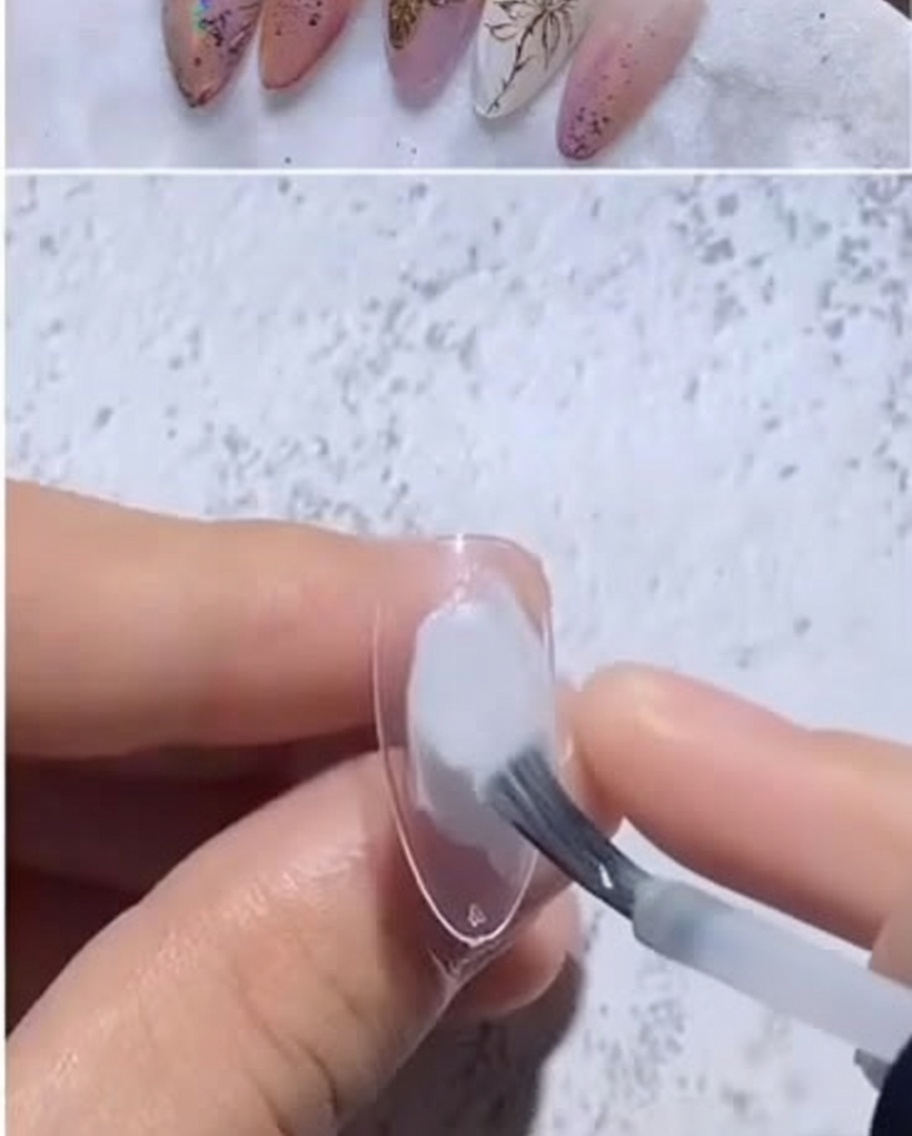 Ein mandelförmiger, klarer Nagel-Tipp erhält einen Tropfen milchig-weißes Gel von einem Pinsel.