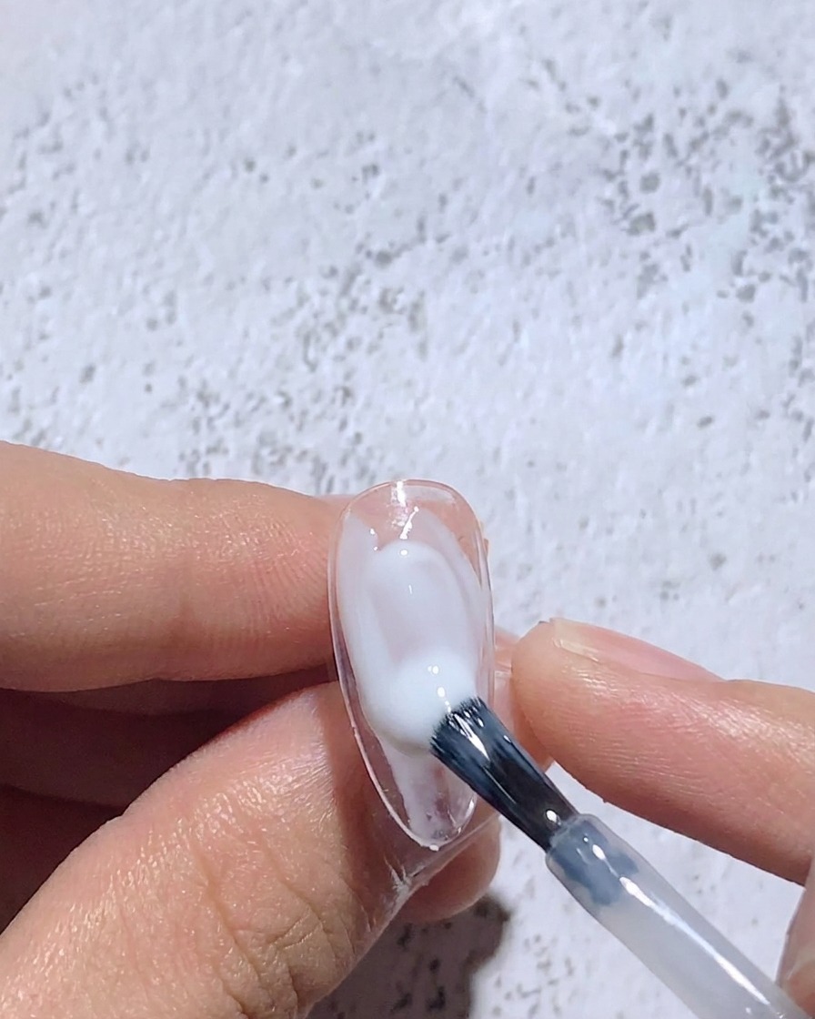 Ein feiner Pinsel verblendet feuchtes, weißes Gel auf einem Nagel-Tipp für ein weiches Zentrum.