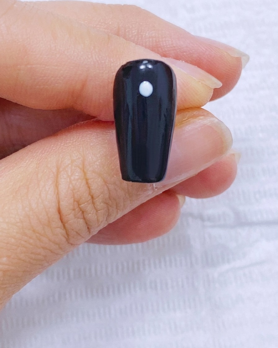 Ein schwarzer Nagel mit einem weißen Mittelpunkt und vier kreisförmig angeordneten äußeren Punkten.