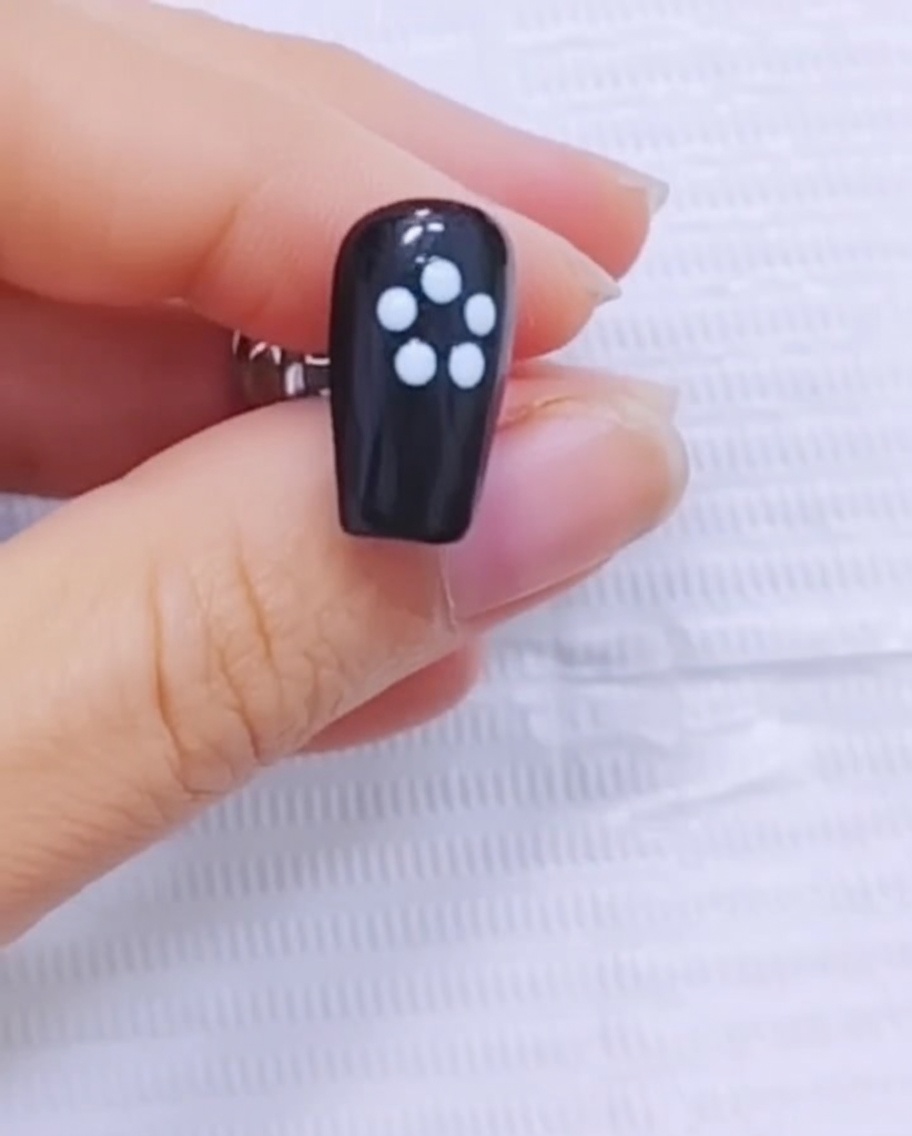 Ein feiner Pinsel zieht weißes Gel vom Mittelpunkt des Blumendesigns nach außen auf einem schwarzen Nagel.