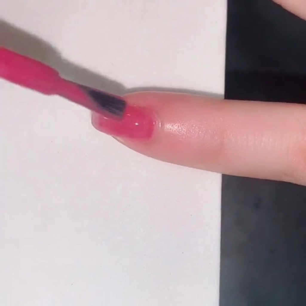 Ein Nagellackpinsel fügt eine dritte Schicht pinkes Jelly-Gel hinzu, um die Farbintensität auf dem Fingernagel zu verstärken.
