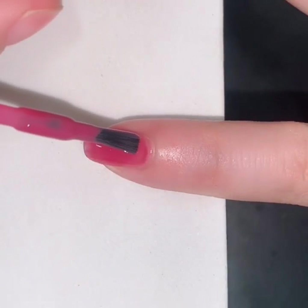 Ein Pinsel trägt einen durchscheinenden pinken Jelly-Lack auf einen Fingernagel auf.