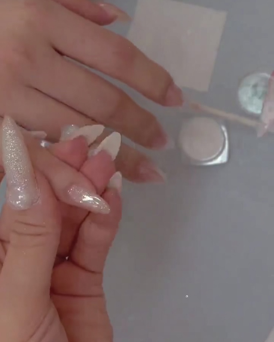 Ein Detailpinsel, der sorgfältig feinen Glitzer über die Basisschicht auf den Nagel aufträgt.