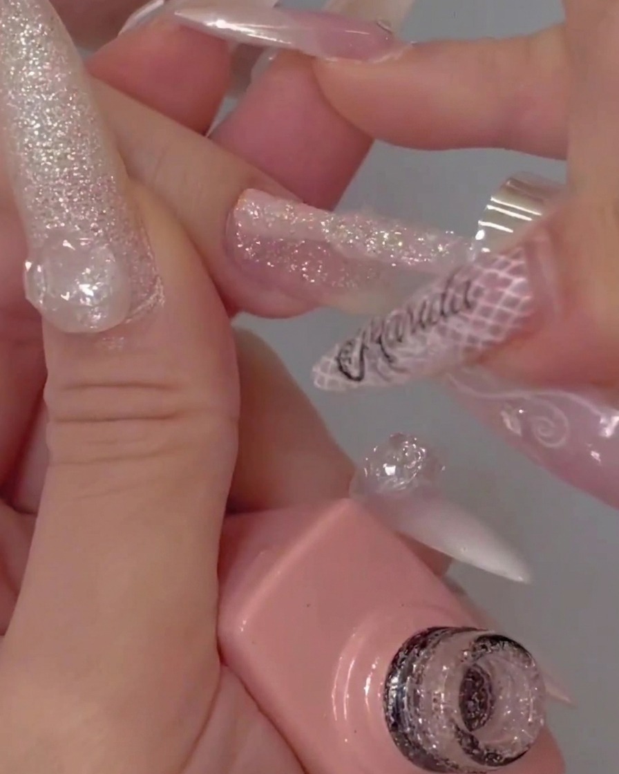 Die Spitze eines Gelpinsels beim Auftragen eines klaren Top Coats über einen strukturierten Glitzernagel.