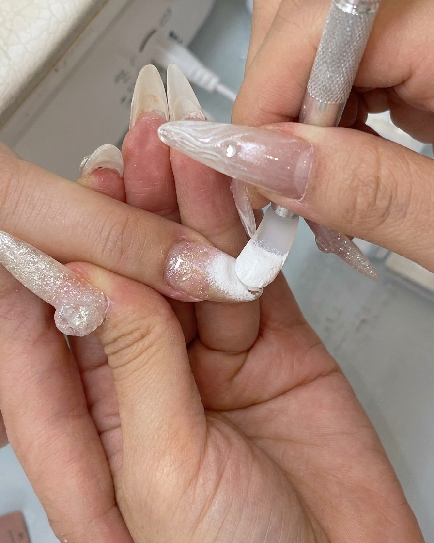 Ein Finger reibt über die Nageloberfläche, um das Chrome-Puder in einen spiegelnden Glanz zu polieren.