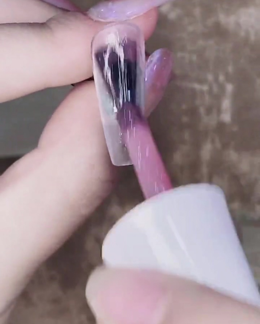 Ein Pinsel trägt eine zweite Schicht transparentes rosa Gel über die erste ausgehärtete Schicht auf.