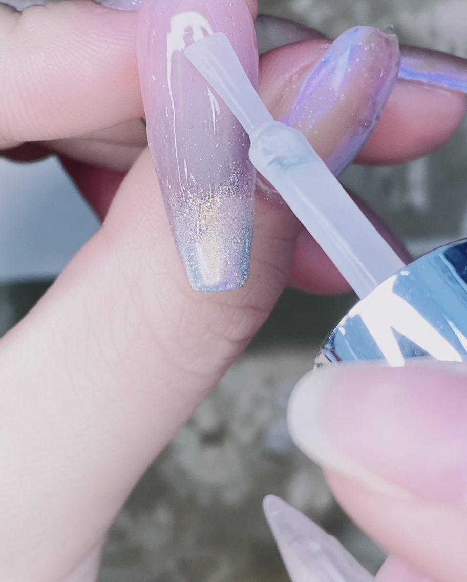 Ein Nagelpinsel trägt klaren Top Coat über den Chrompuder-Verlauf auf.