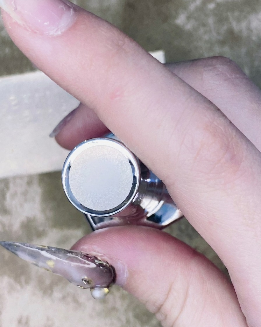 Ein feiner Nail-Art-Pinsel trägt einen kleinen Tropfen Top Coat um die Basis eines Strasssteins auf.