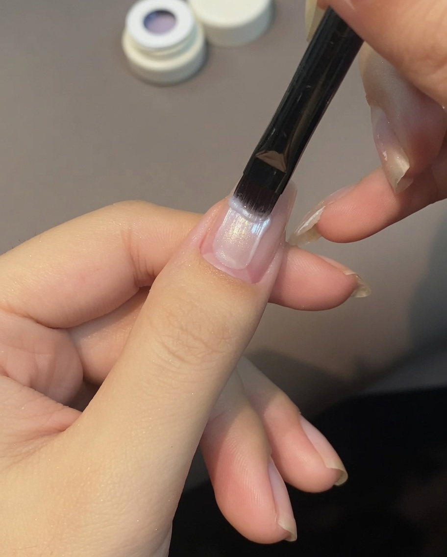 Ein Pinsel trägt helllila Cat Eye Gel über einen Fingernagel auf.