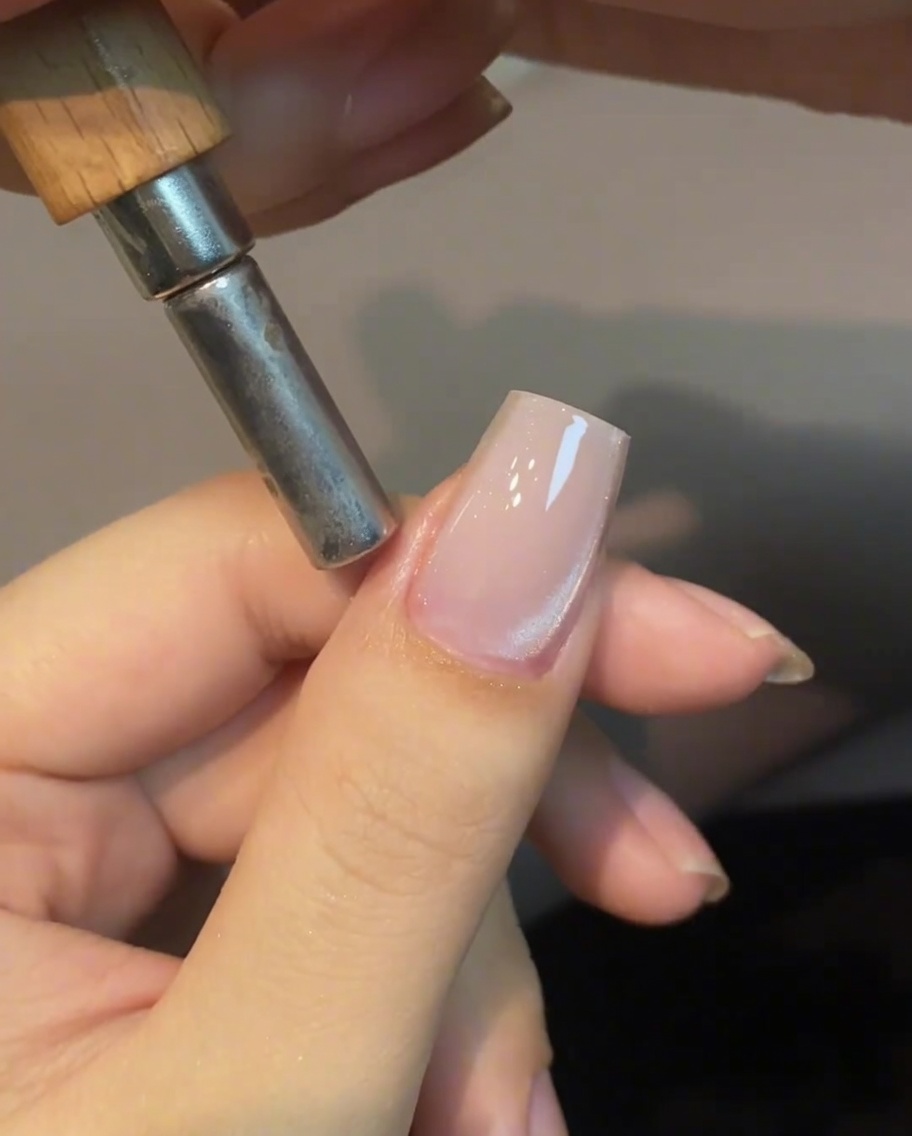 Ein zylindrischer Magnet wird nahe der Seite eines Fingernagels gehalten, um den Cat-Eye-Schimmer zu manipulieren.