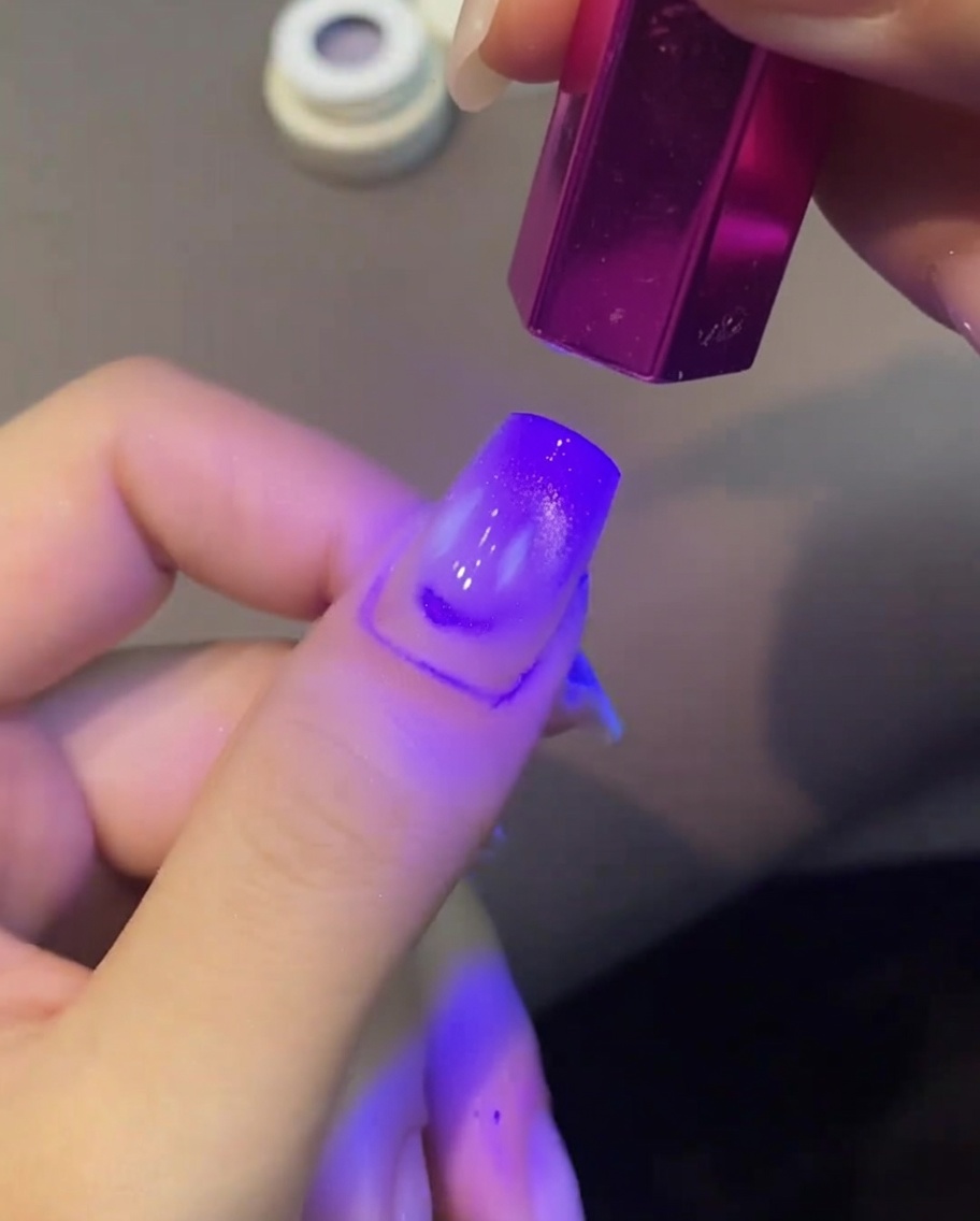 Ein lila Cat Eye Gelnagel wird unter einer kleinen violetten UV-Handlampe ausgehärtet.