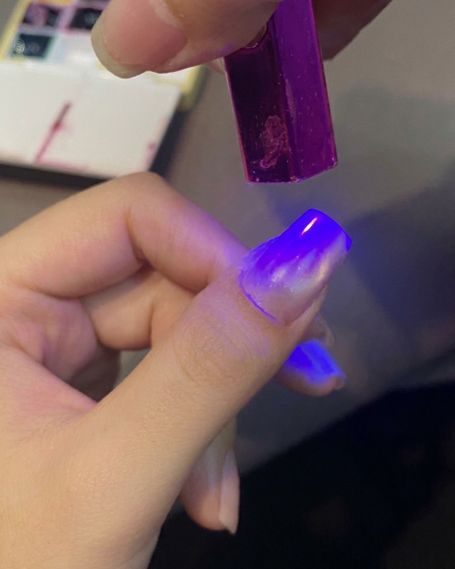 Ein Fingernagel wird unter einem violetten Mini-UV-Licht ausgehärtet, um ein Geldesign zu fixieren.
