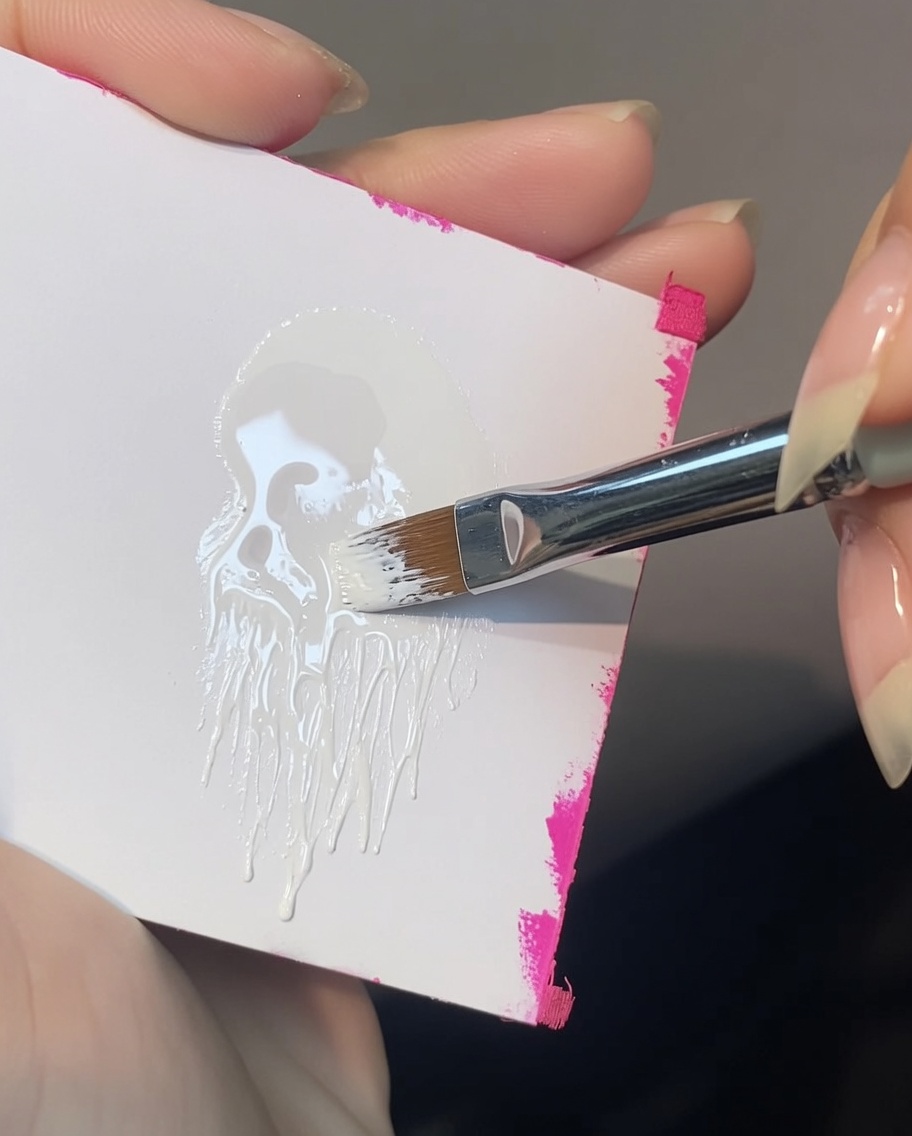 Ein abgeschrägter Nail-Art-Pinsel nimmt weißes Painting Gel von einer Palette auf, wobei nur eine Ecke der Borsten beladen wird.