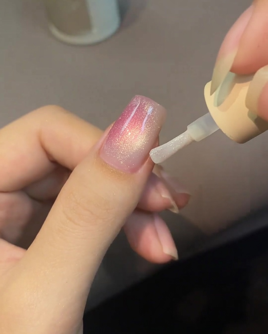Eine Nahaufnahme einer Nageloberfläche, auf der kleine, perlmuttfarbene Wassertropfen auf einer nassen Top-Coat-Basis aufblühen.