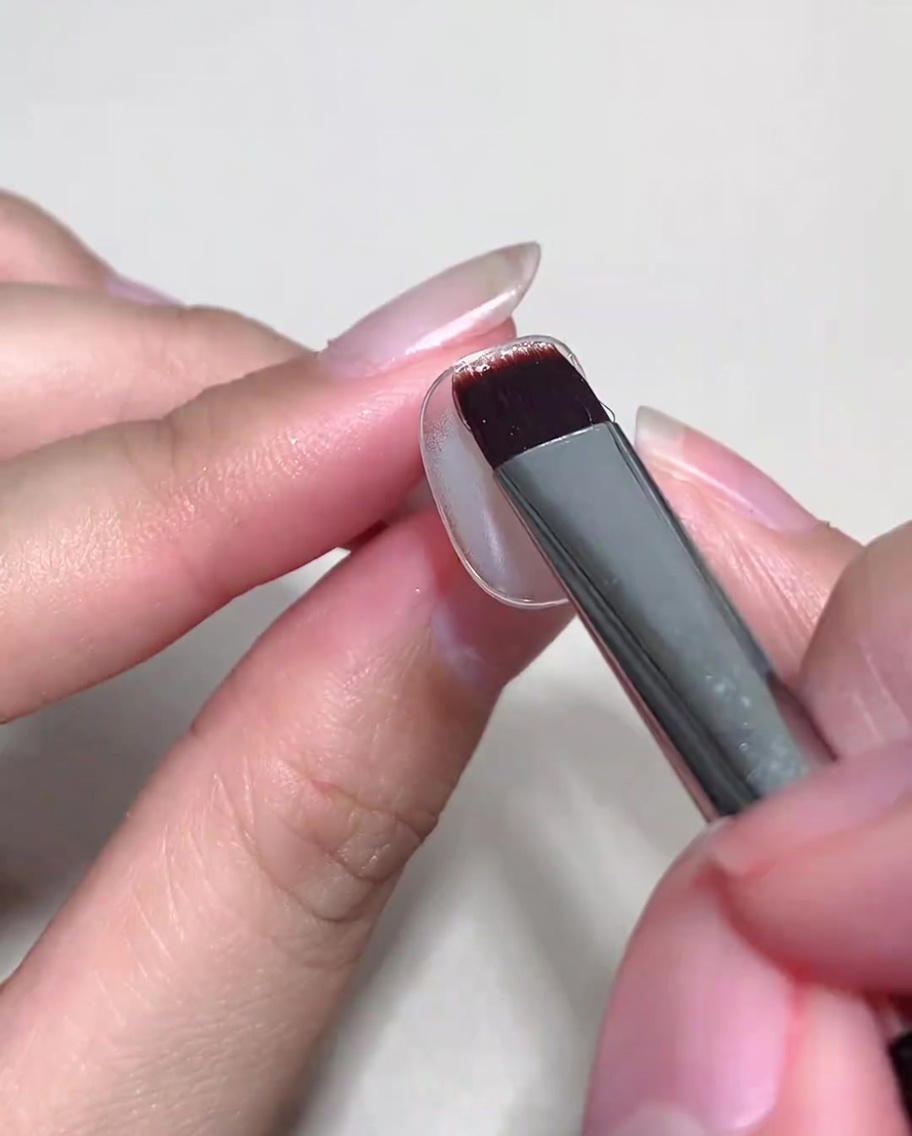 Ein Pinsel trägt eine Schicht Nude Cat-Eye-Gel auf einen bereits grundierten Nagel auf.