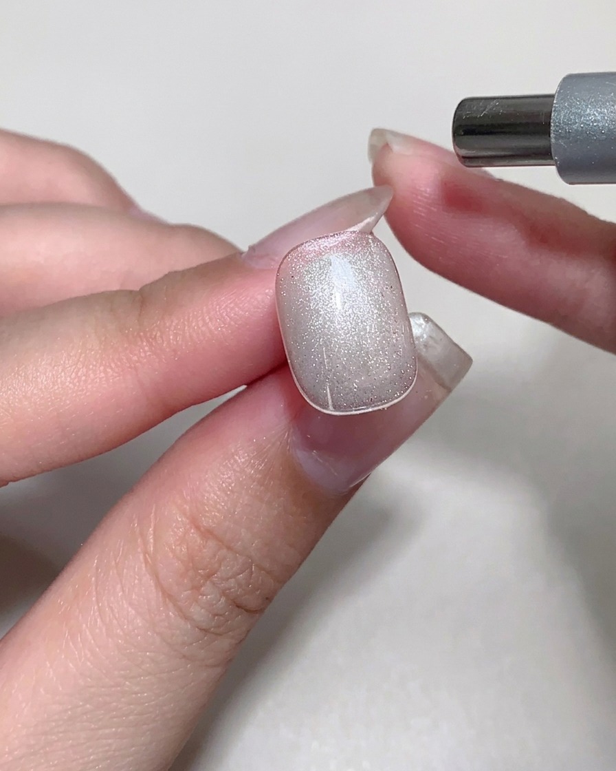 Ein Magnet wird über einem Nagel mit feuchtem Cat-Eye-Gel verwendet, um einen glasartigen Schimmereffekt zu erzeugen.