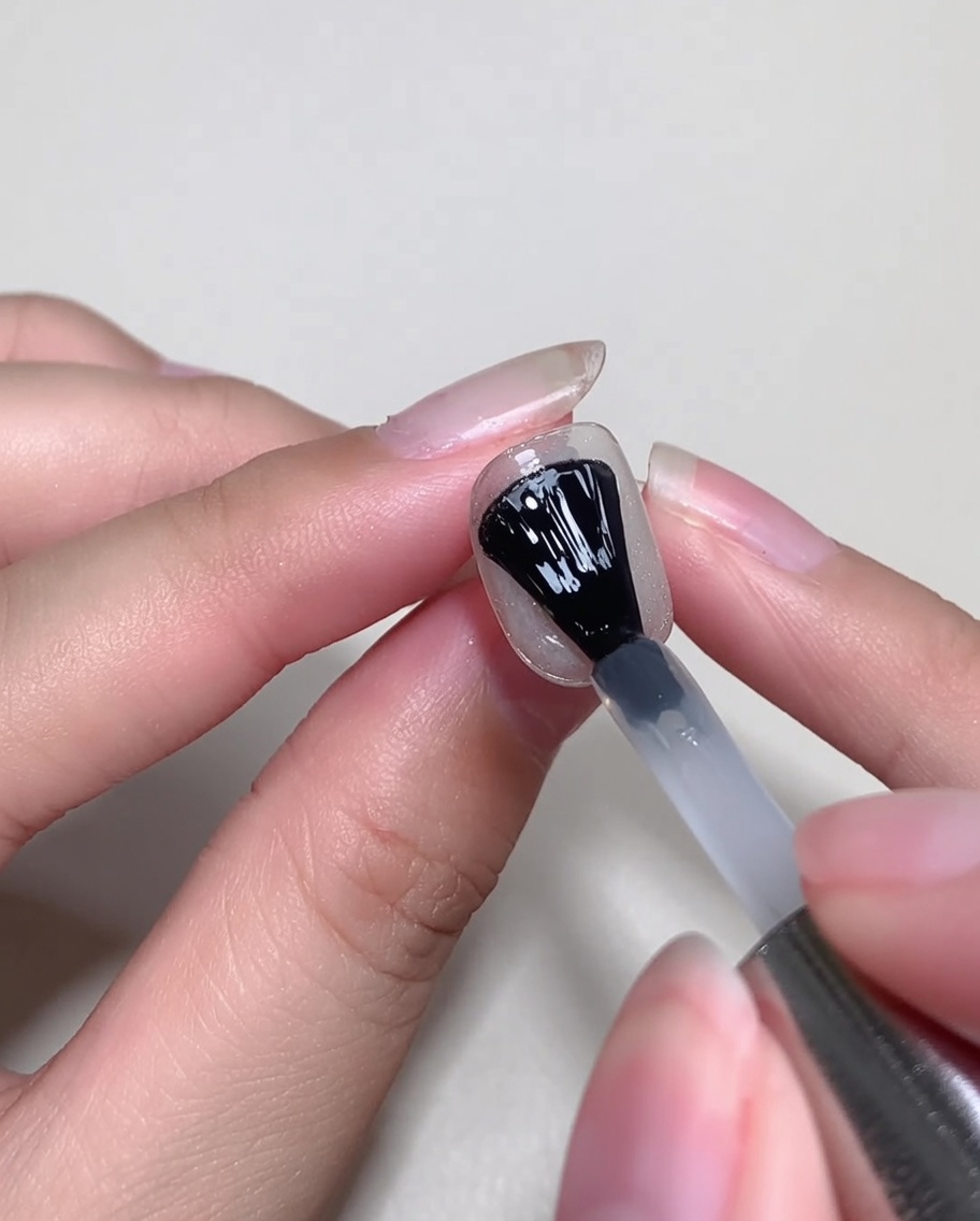 Ein Gelpinsel trägt eine dünne Schicht klares Blooming-Gel über einen dekorierten Nagel auf.