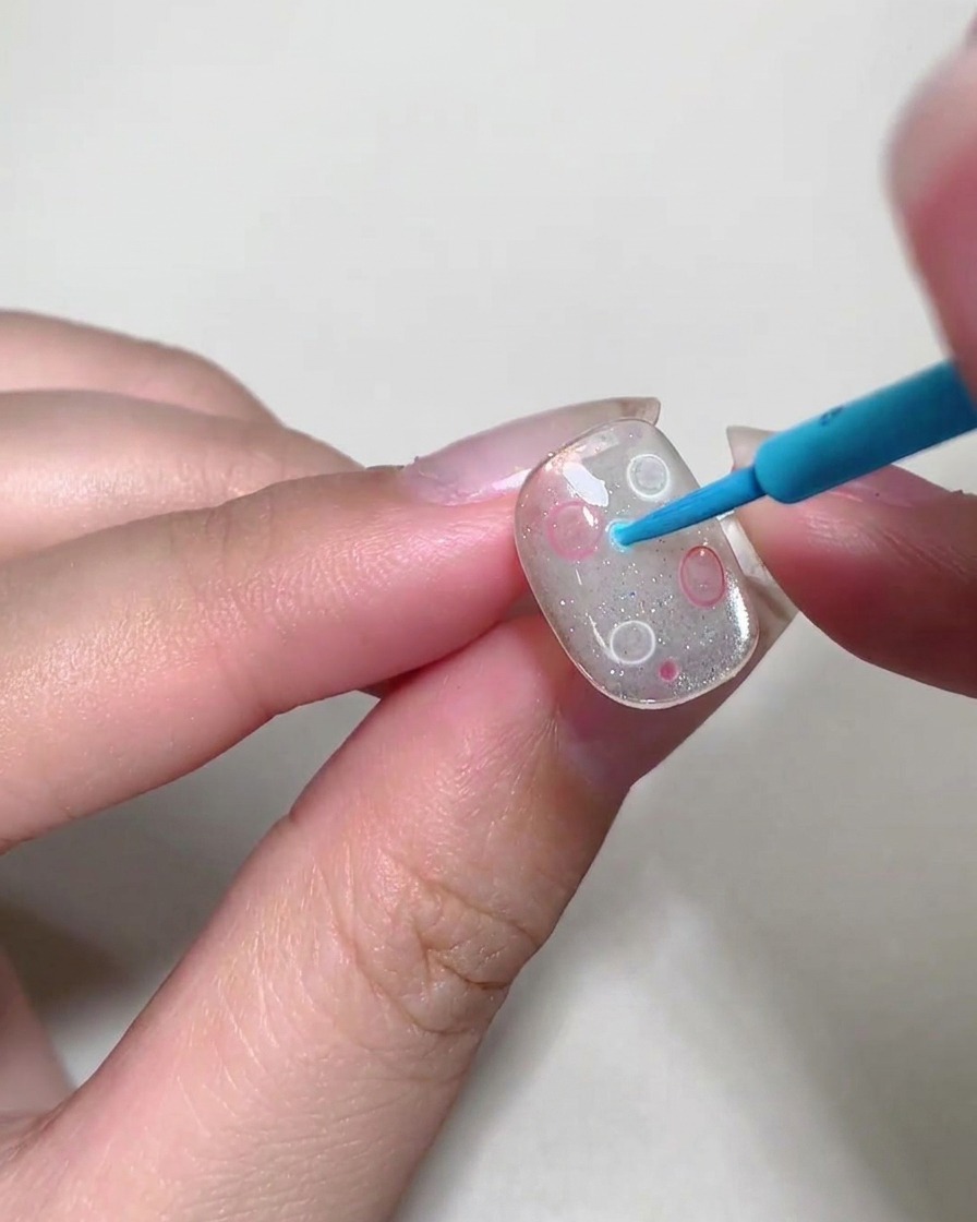 Ein Dotting-Tool platziert kleine, bunte Flüssigkeitsblasen auf einer Nageloberfläche.