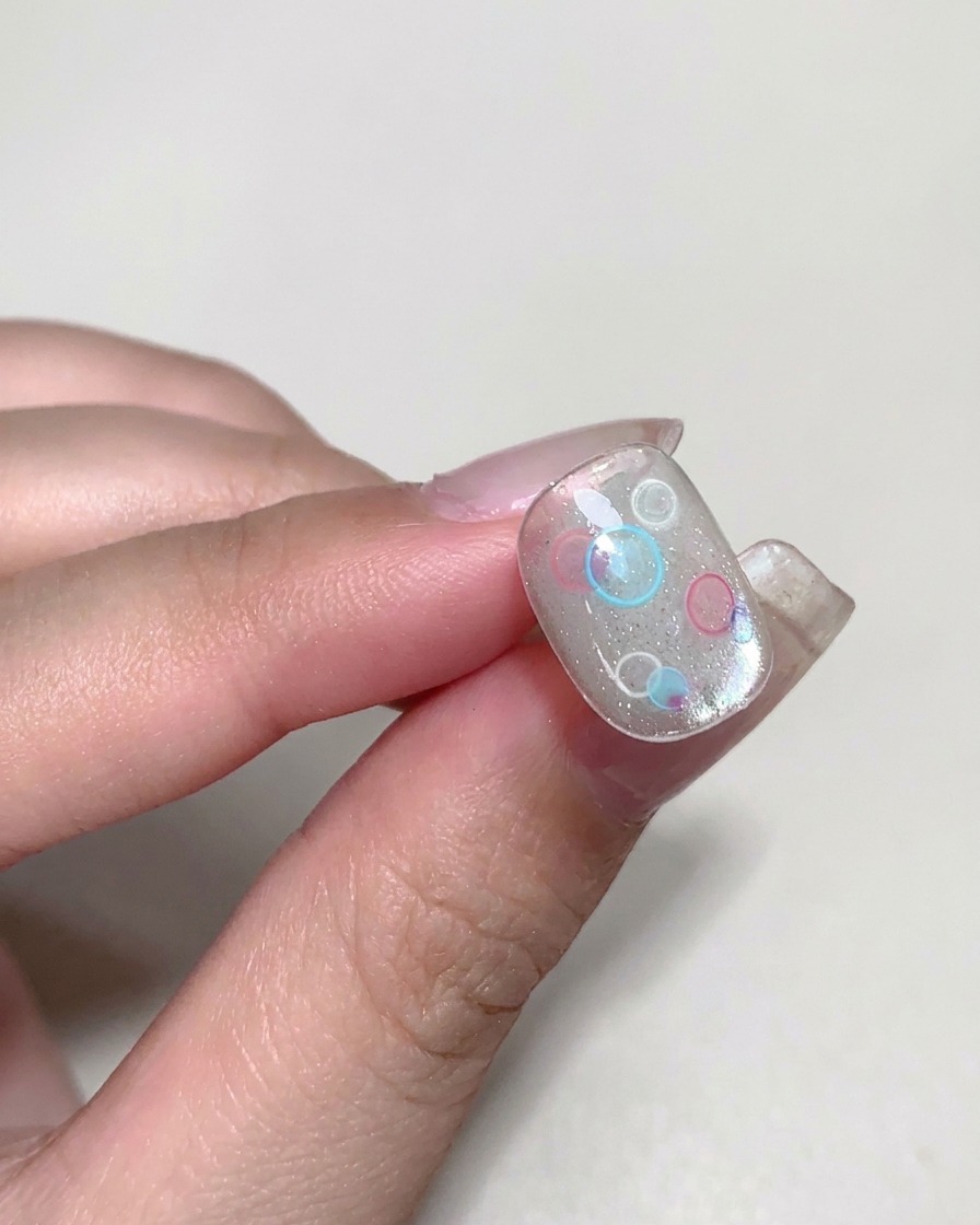 Ein Pinsel trägt klares, viskoses Builder-Gel über einem dekorierten Nagel auf.
