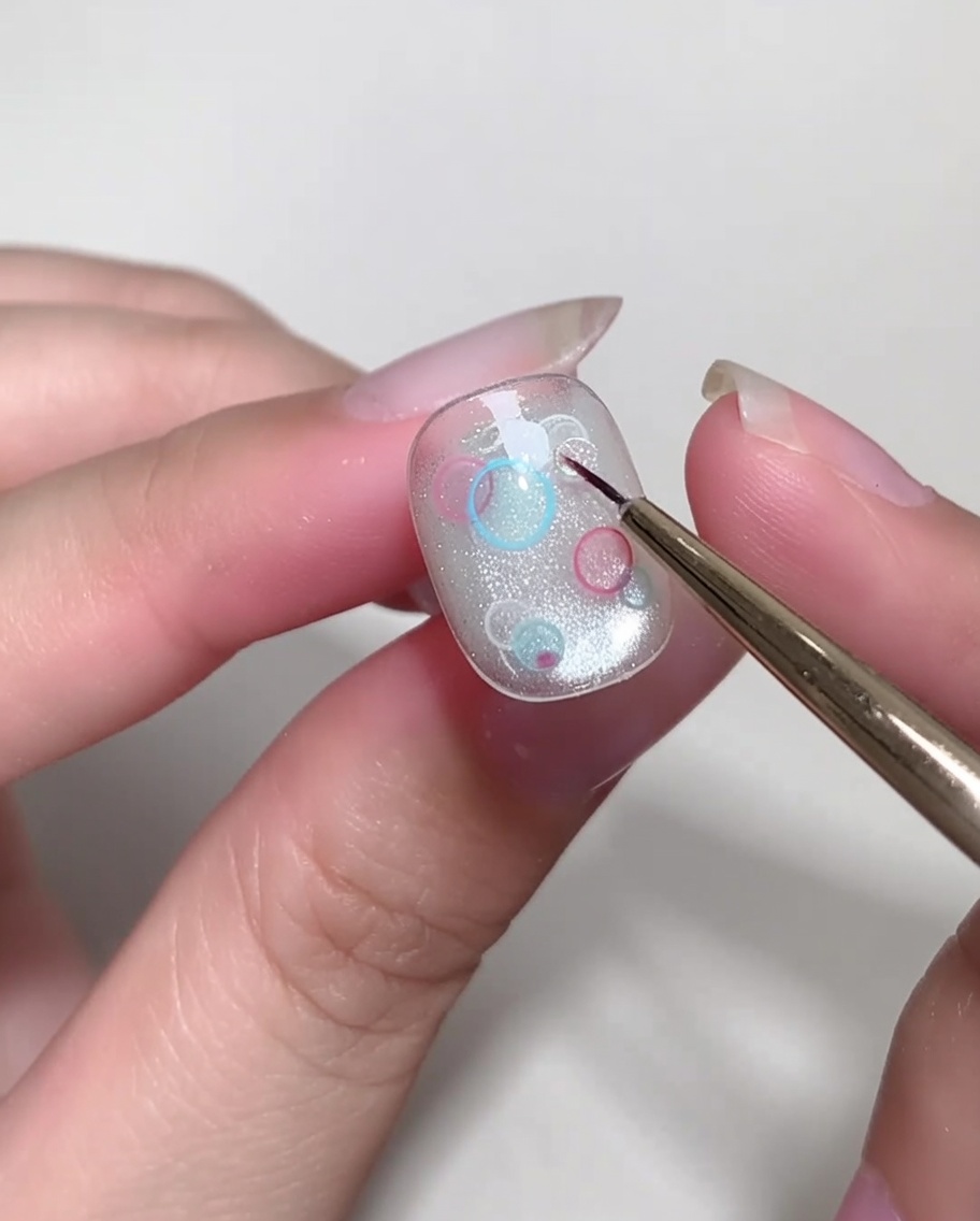 Ein feiner Pinsel platziert sorgfältig kleine, klare, runde Pailletten auf einem Nagel.