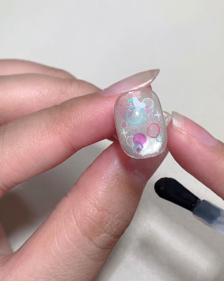 Ein Pinsel trägt einen glänzenden Top Coat auf die Nageloberfläche auf.