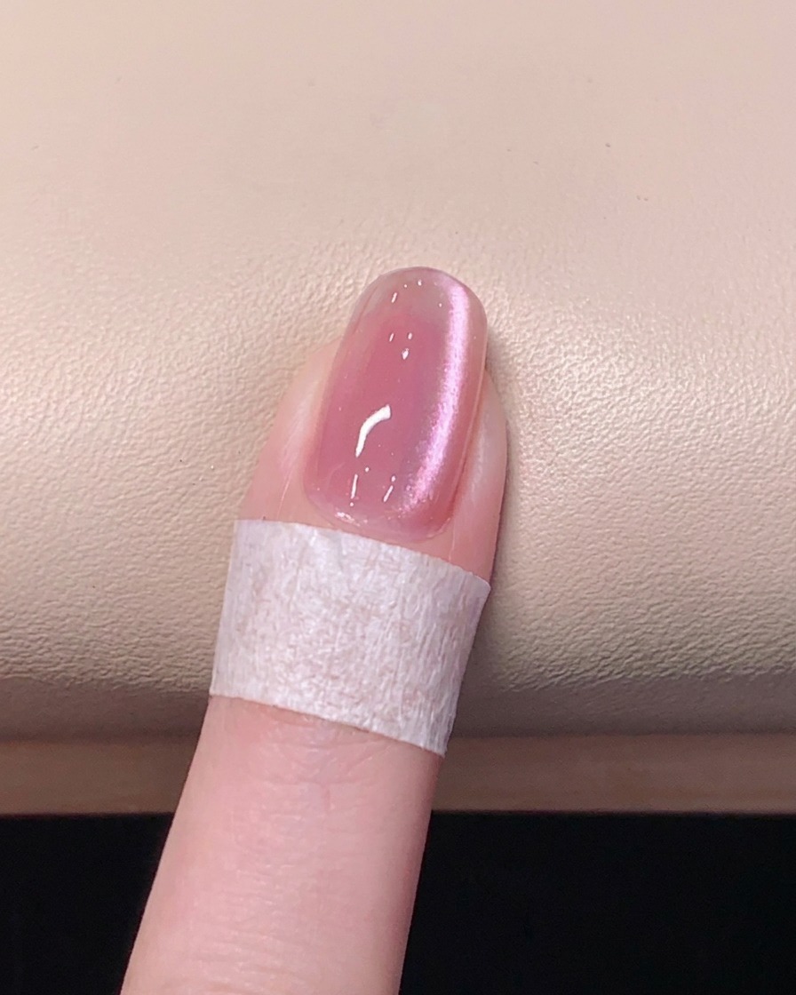 Ein Pinsel trägt einen klaren, glänzenden Überlack auf einen pinken magnetischen Cat-Eye-Gel-Nagel auf.
