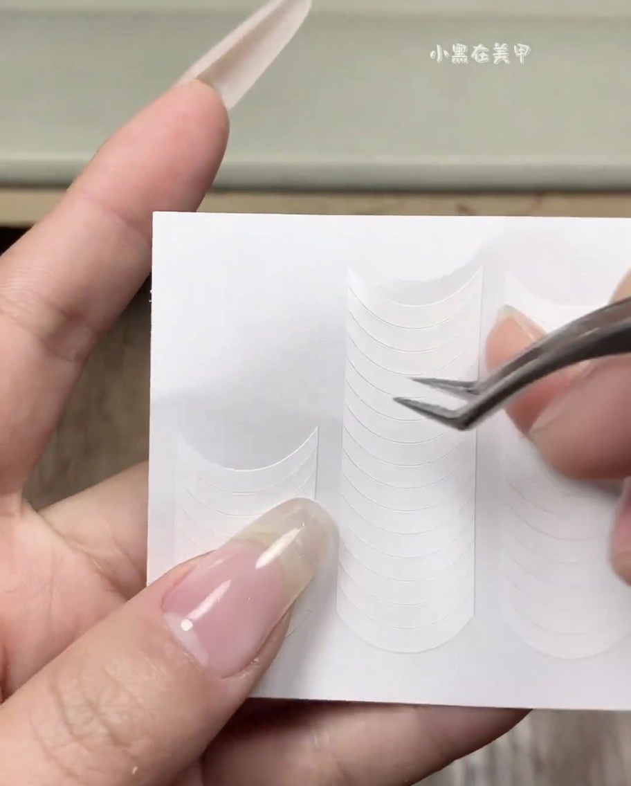 Hand, die einen weißen French-Tip-Aufkleber auf einem sauberen, natürlichen Fingernagel anbringt.
