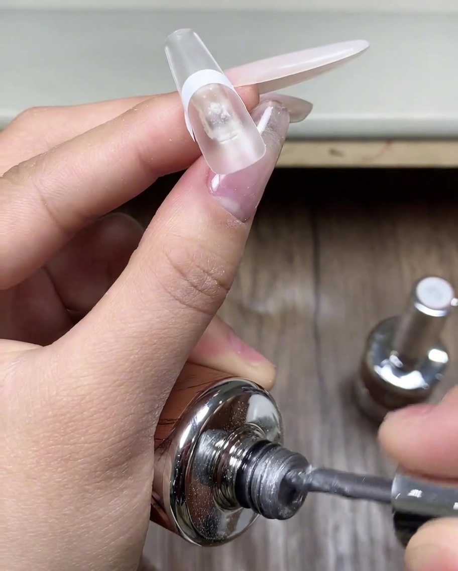 Pinsel, der eine Schicht graues Cat-Eye-Gel auf den Bereich hinter dem Aufkleber aufträgt.