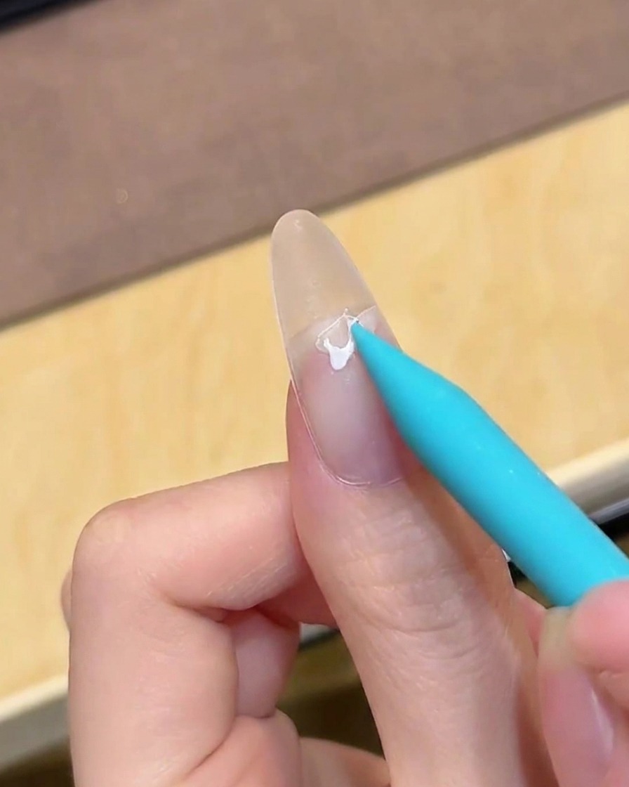 Ein Pinsel trägt klaren Base Coat auf einen vorbereiteten, nackten Nagel auf.
