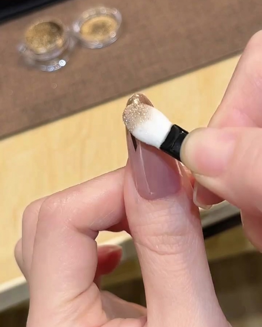 Ein Schwämmchen-Applikator poliert Gold-Chrome-Puder auf die Spitze des Nagels.