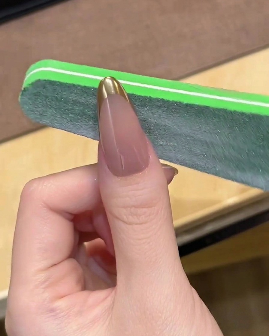 Eine Nagelfeile glättet vorsichtig die Spitze einer Chrome-French-Maniküre.