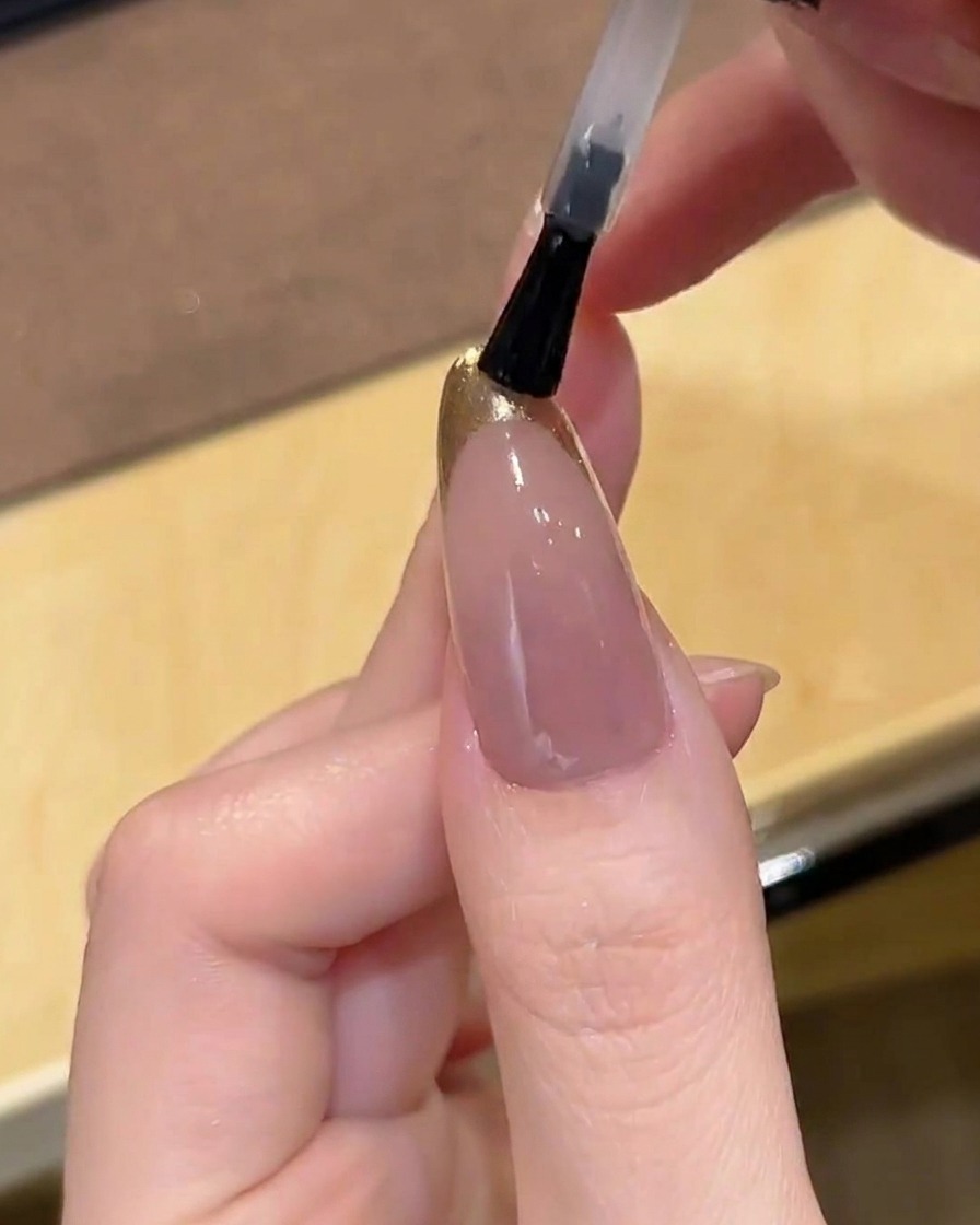 Ein Pinsel trägt einen glänzenden Top Coat auf den Gold-Chrome-French-Tip auf.