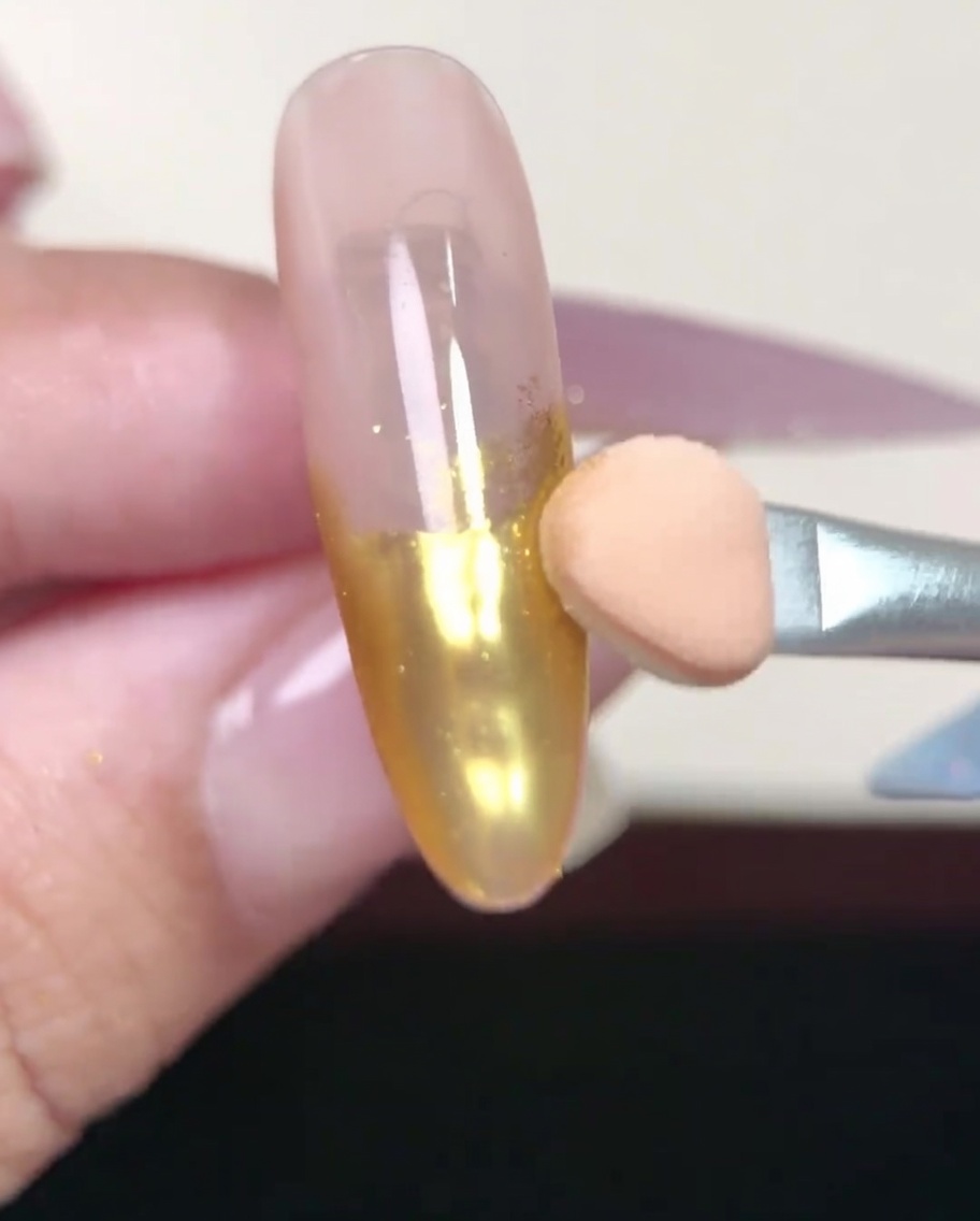 Ein Nagelpinsel trägt sanft eine Schicht Nude-Gel-Base-Coat auf einen vorbereiteten mandelförmigen Nagel auf.