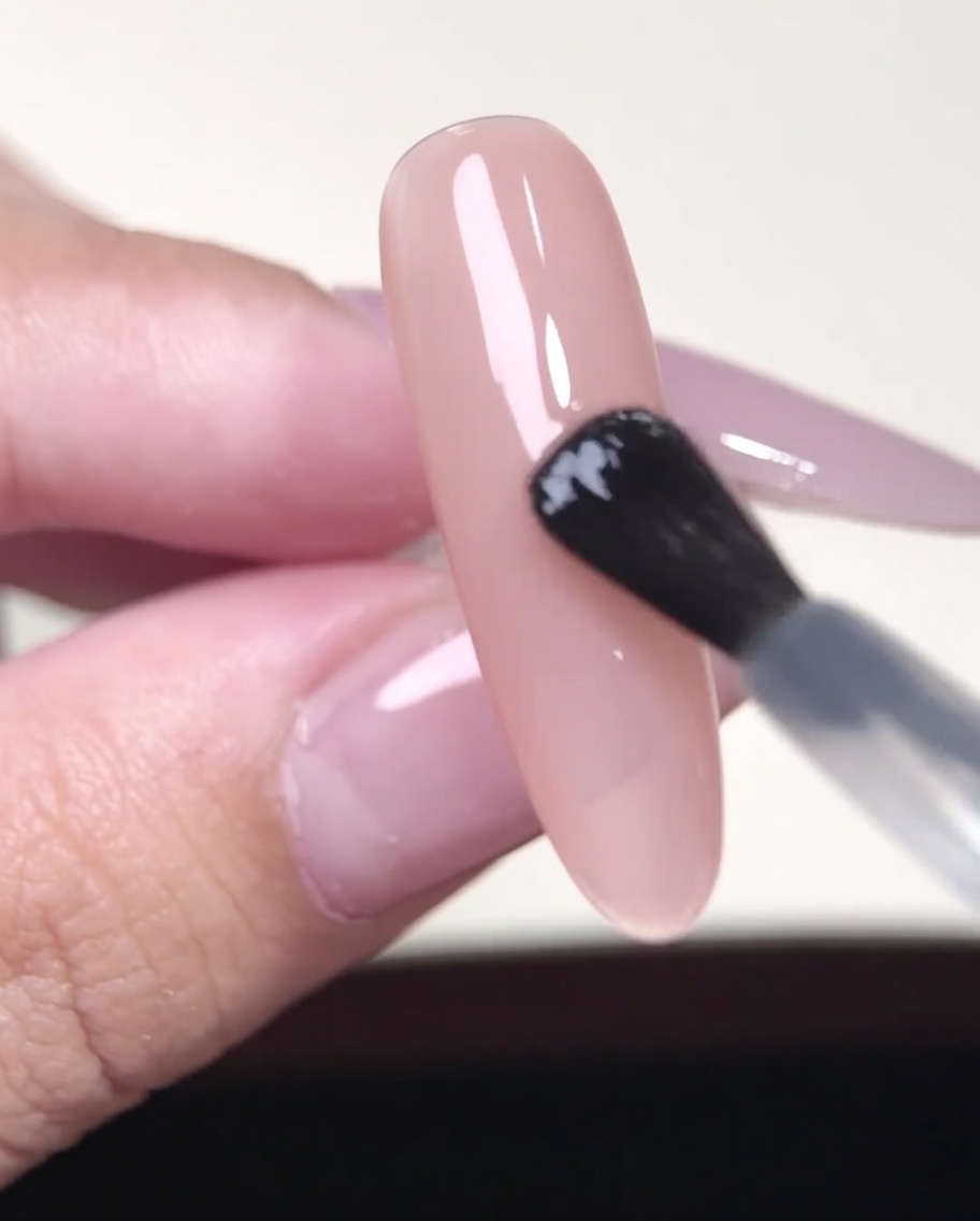Eine Pinzette hält einen French-Tip-Sticker über einen nudefarbenen Gelnagel.