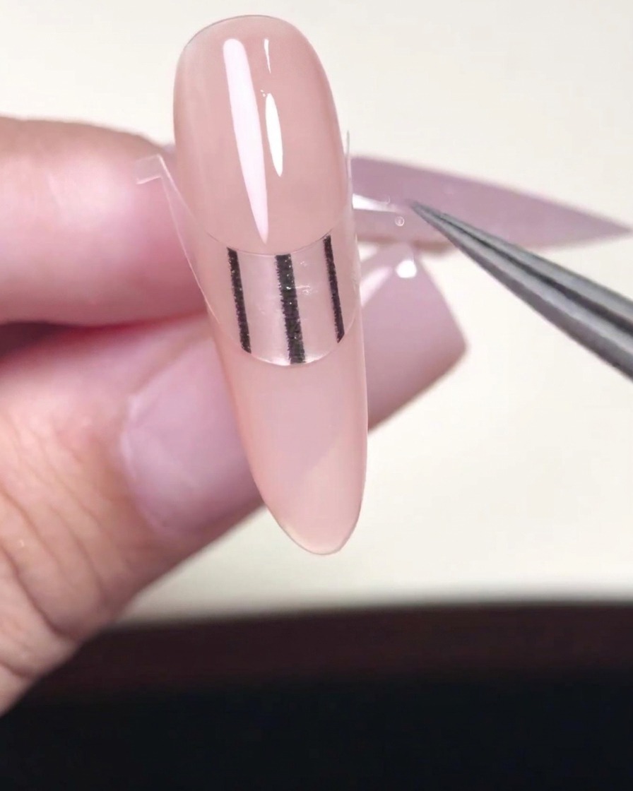 Ein Metallwerkzeug drückt die Ränder eines French-Tip-Stickers fest auf einen mit Gel lackierten Nagel.