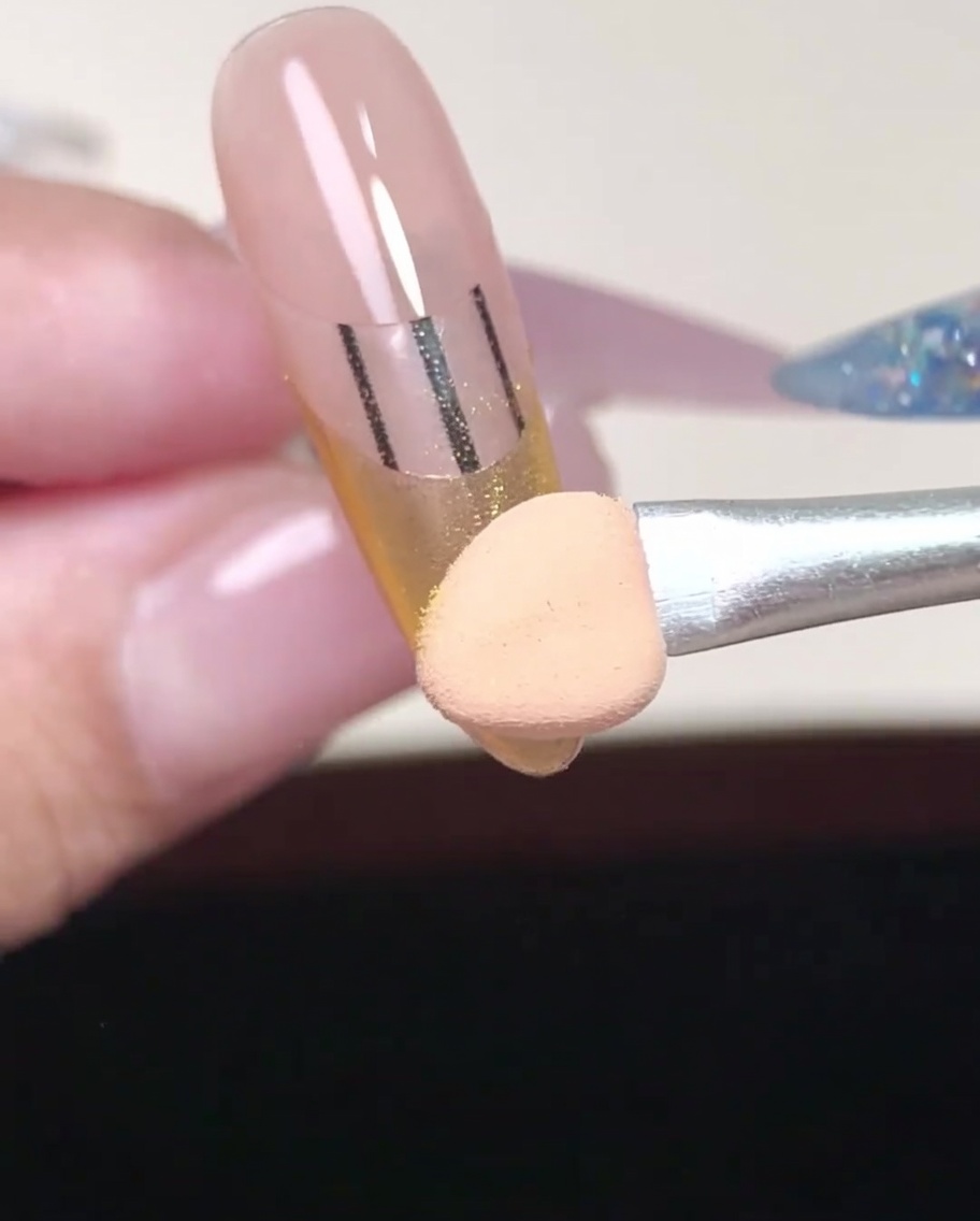 Nahaufnahme der Applikatorspitze, die goldenes Puder in die Ecken des French-Tip-Bereichs einarbeitet.