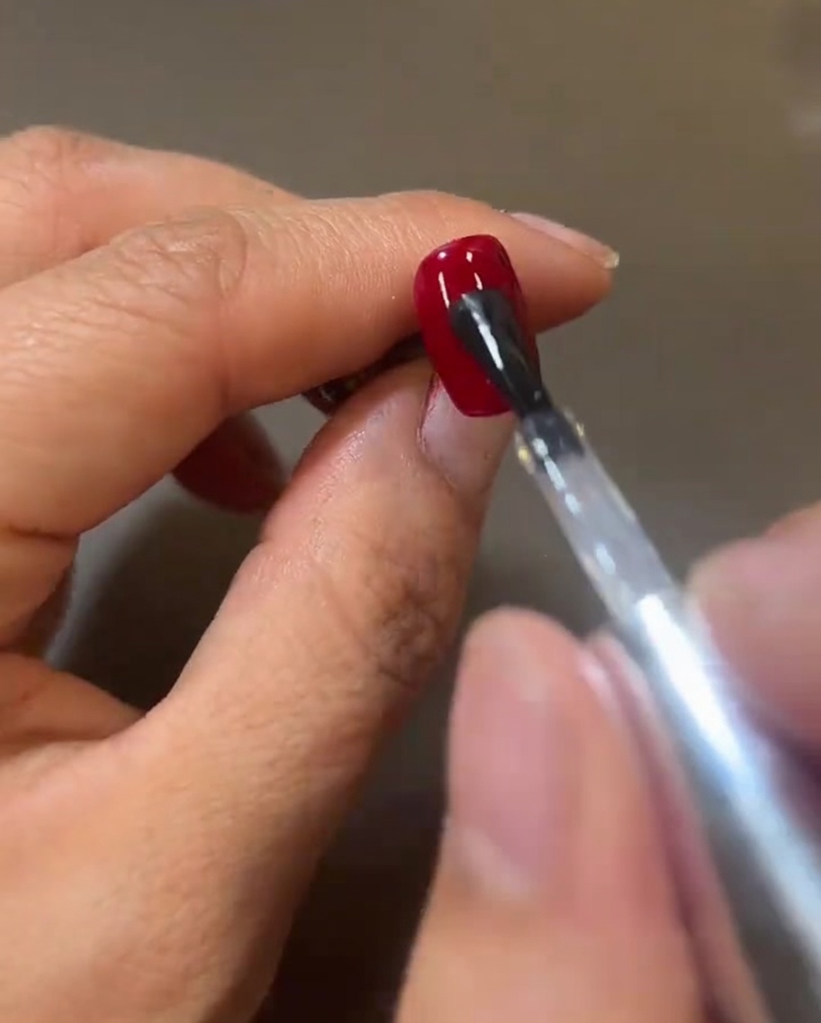 Ein Nagelpinsel trägt eine frische, glänzende Schicht Top Coat auf das rote Gel auf und erzeugt eine nasse, reflektierende Oberfläche.