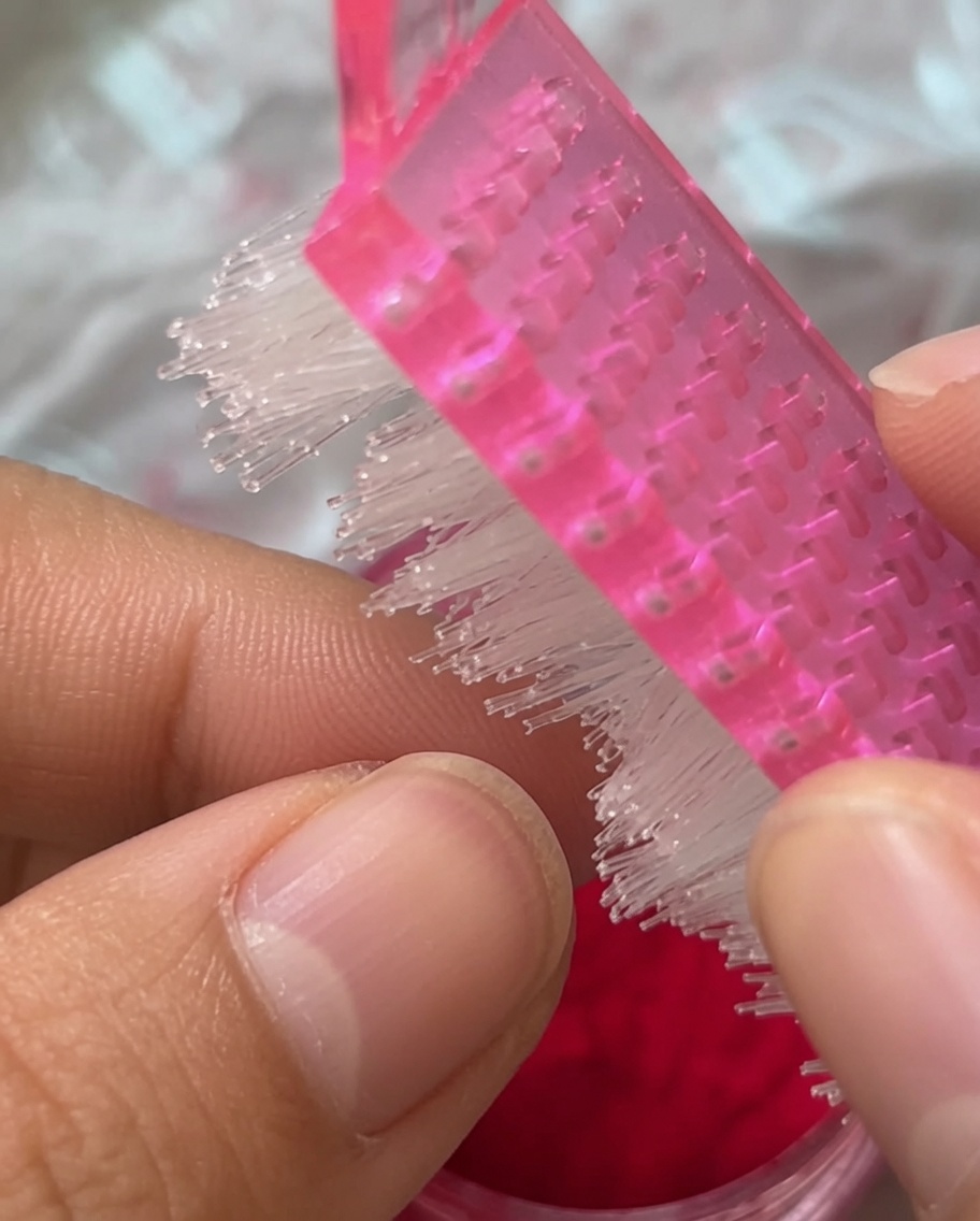 Nahaufnahme eines rosafarbenen Nagelpinsels, der über einen mit Plüsch bedeckten roten Nagel streicht.
