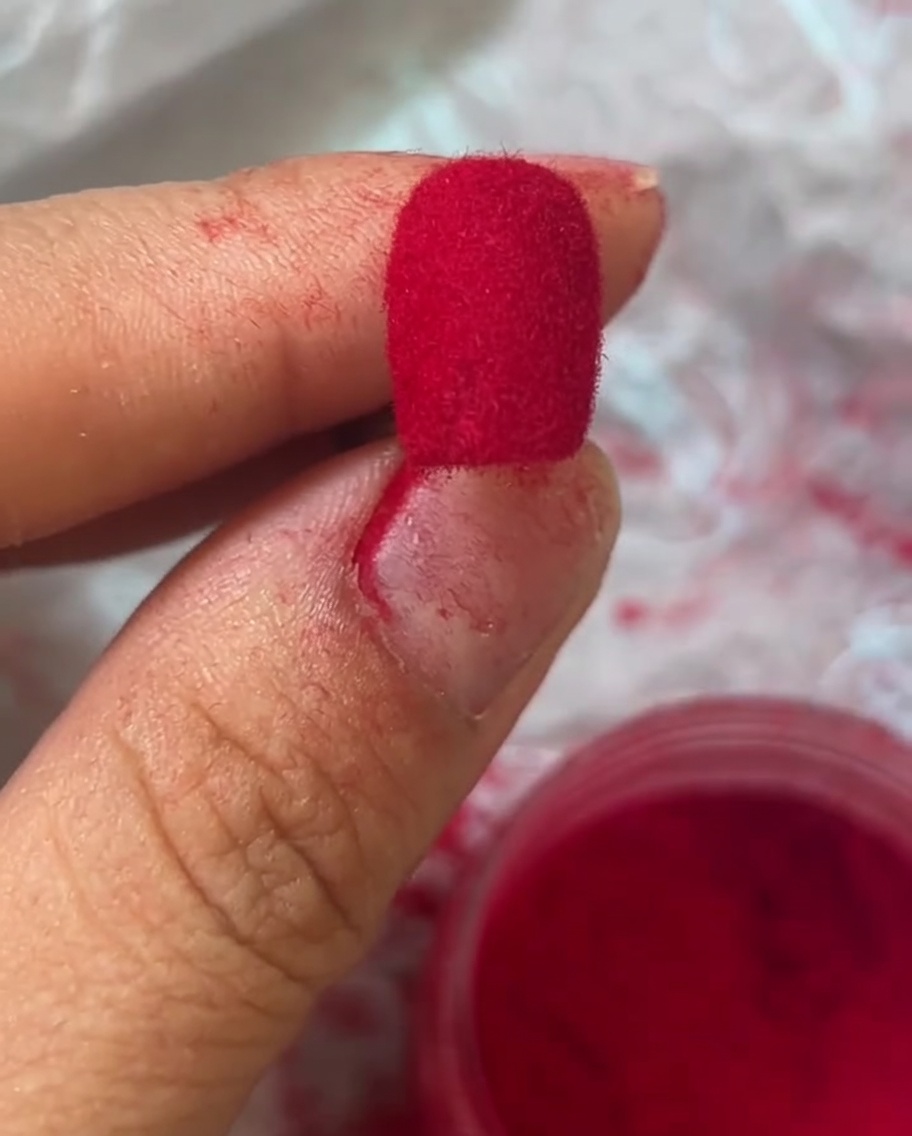 Makroaufnahme eines Fingernagels, der mit einem leuchtend roten Samt-Finish bedeckt ist.