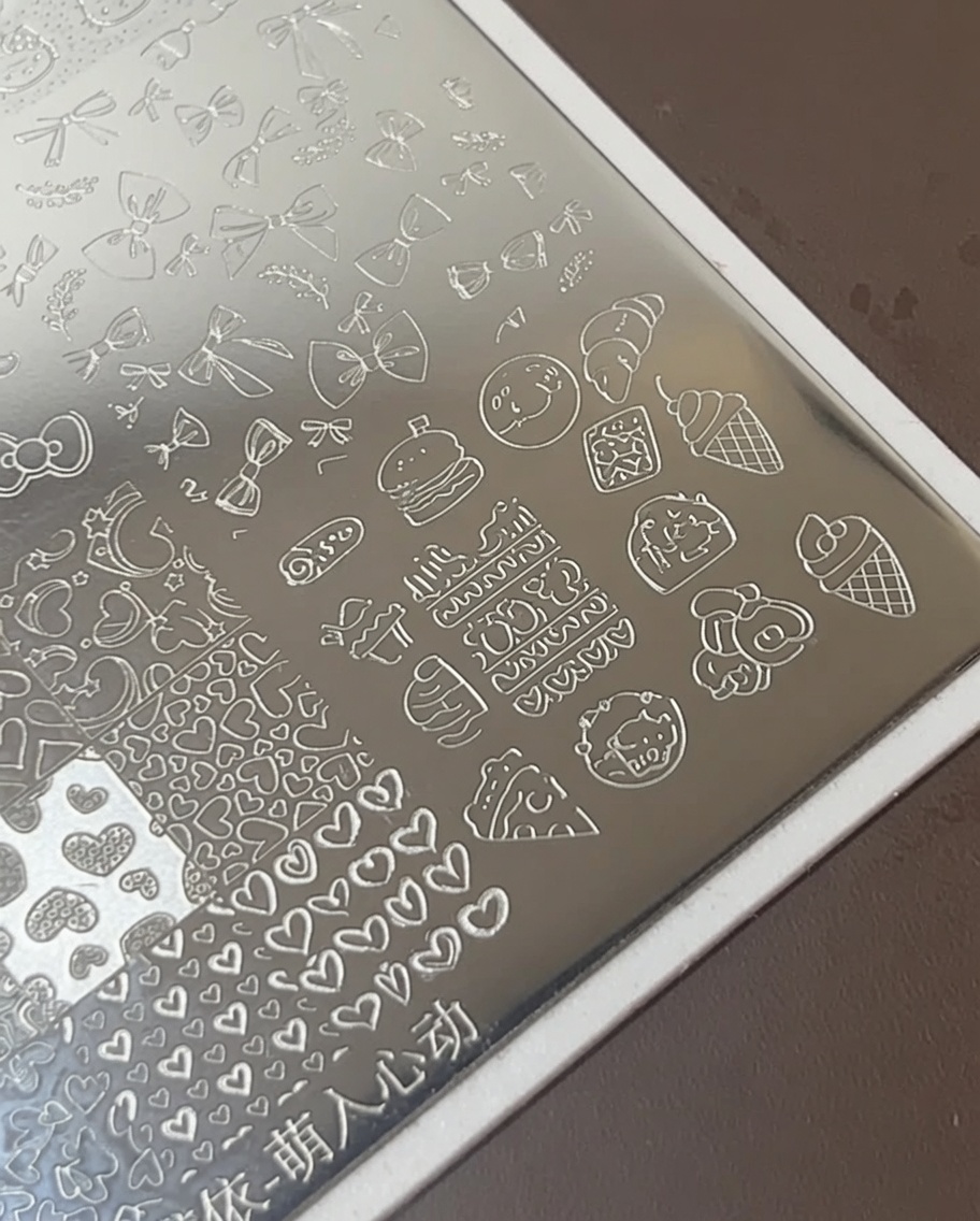 Ein Nagelkunst-Pinsel trägt dicken weißen Lack über geätzte Food-Symbole auf einer Metall-Stamping-Platte auf.