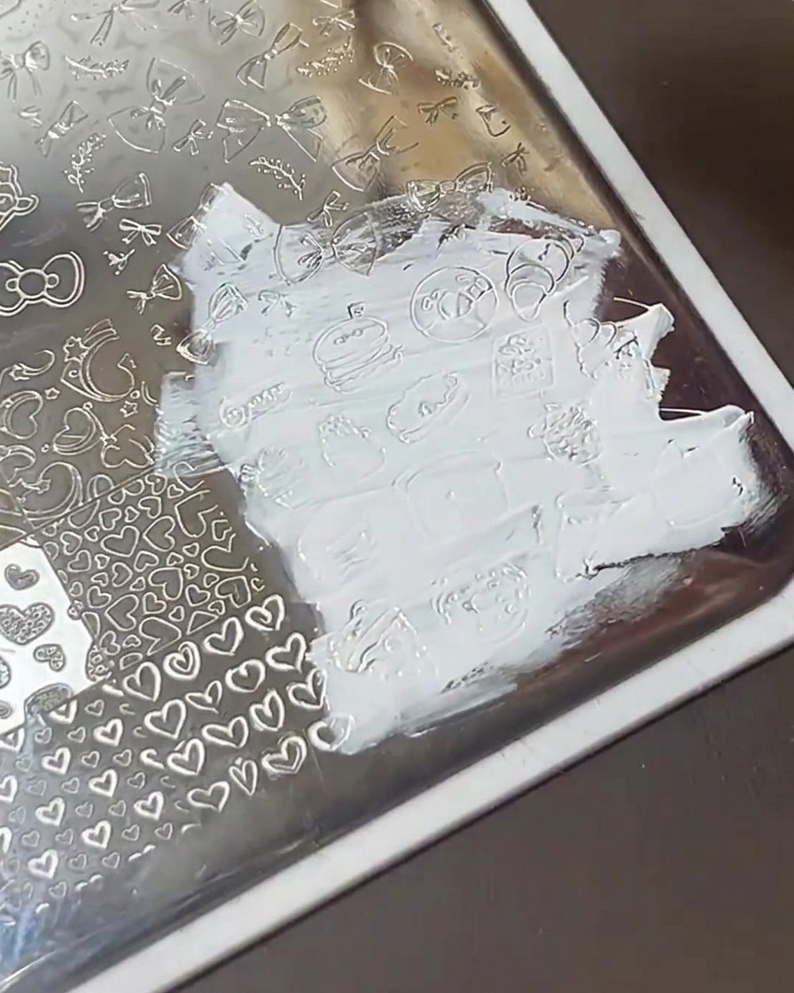 Eine transparente Plastikkarte wischt über eine Metall-Stamping-Platte und hinterlässt saubere, mit weißem Lack gefüllte Designs.