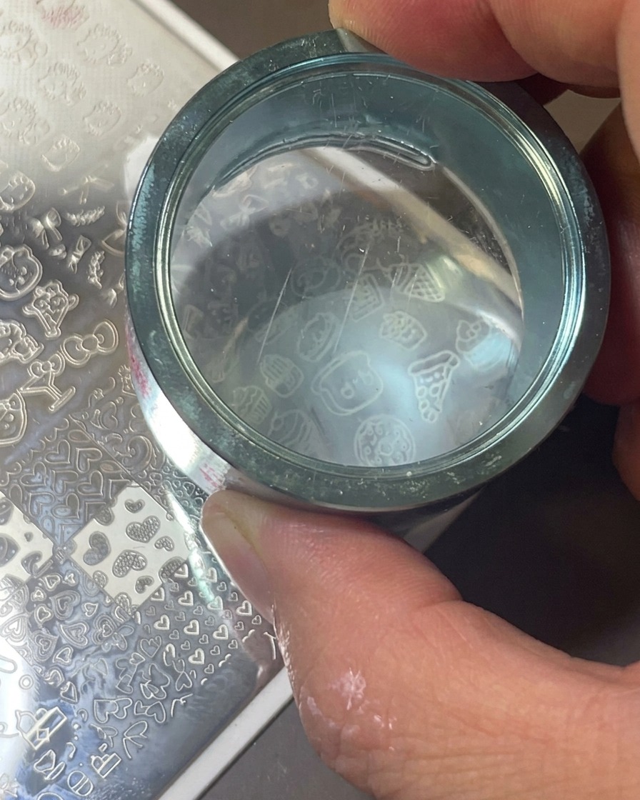 Ein durchsichtiger Silikonstempel wird auf eine Metallplatte gedrückt, um das weiße Icon-Design aufzunehmen.