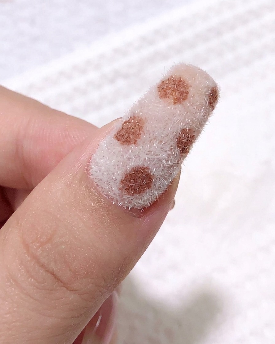 Eine Nahaufnahme zeigt einen feinen Liner-Pinsel beim Auftragen von schwarzem Gel, um Leopardenflecken auf der strukturierten Nageloberfläche zu zeichnen.